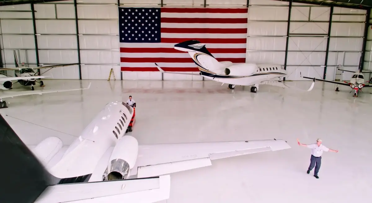 Luxury private jets displayed in pristine American hangar with large flag backdrop and ground crew