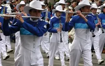 Marching band in white uniforms and hats performing at rodeo event with flutes and instruments