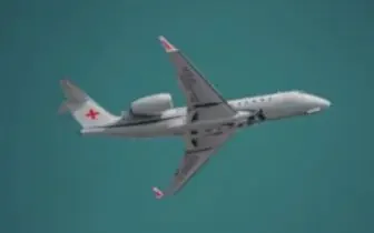 Medical air ambulance aircraft with red cross markings flying against teal sky for emergency transport