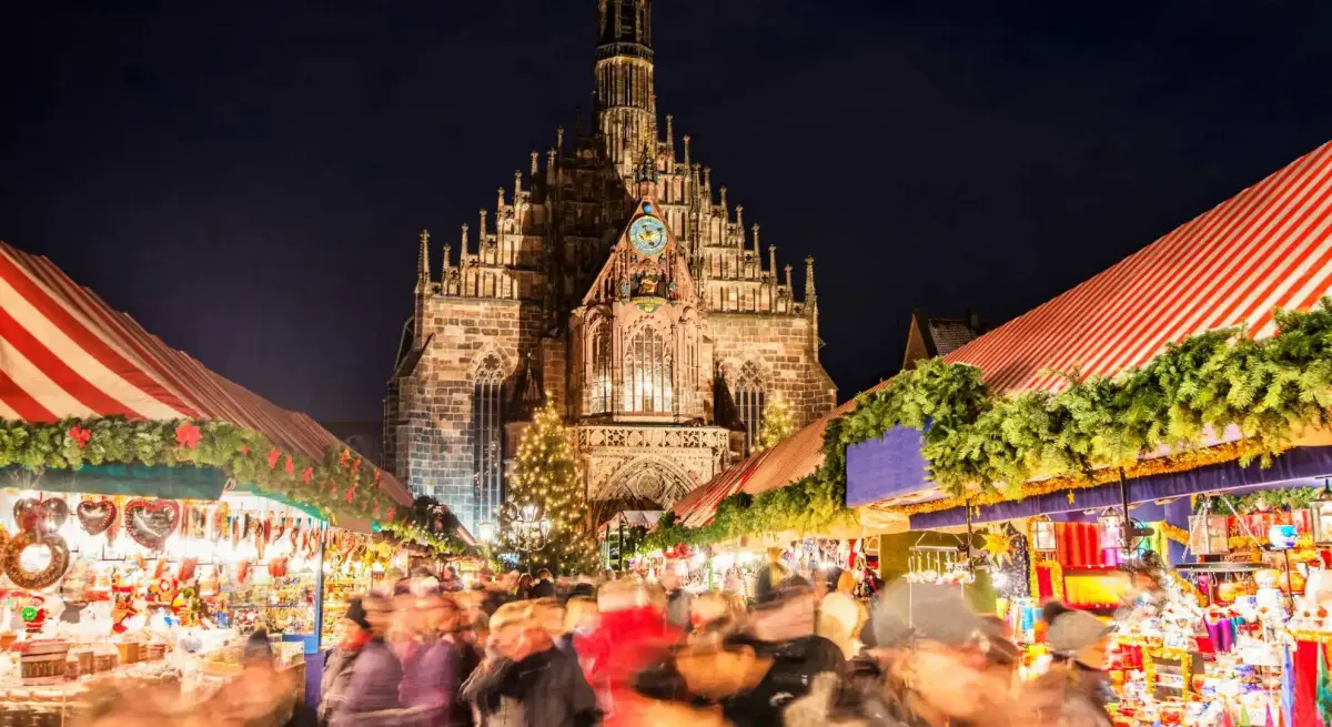 Nuremberg Christmas market bustling with visitors beneath illuminated Gothic church spires on winter evening