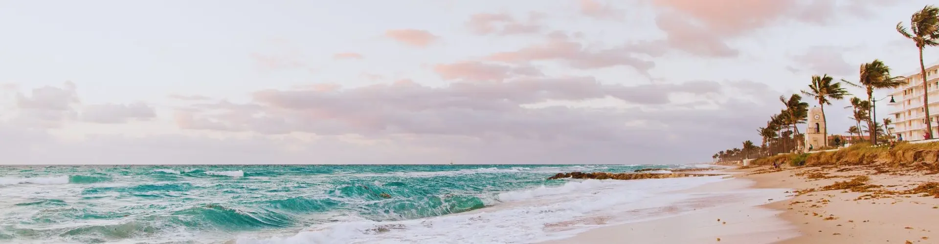 Pristine tropical beach with turquoise waves and palm trees under soft pink sunset sky for luxury travel
