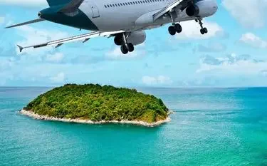 Private jet approaching tropical island paradise with turquoise waters and lush green coastline