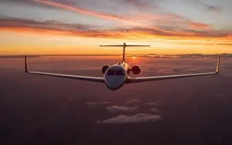 Private jet flying above clouds at sunset showcasing sleek aircraft design for UK aviation types
