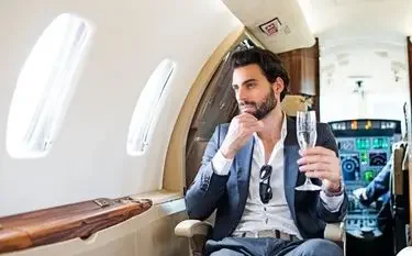 Booking a Private Jet for Business Travel in the UK Professional businessman enjoying champagne while working on laptop during luxury private jet flight