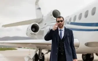 Professional businessman in suit speaking on phone beside luxury private jet on airport tarmac