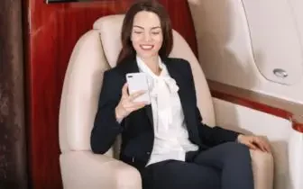 Professional businesswoman enjoying luxury private jet cabin comfort while working on mobile device