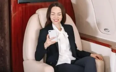 Professional businesswoman relaxing in luxury private jet cabin while using smartphone during flight