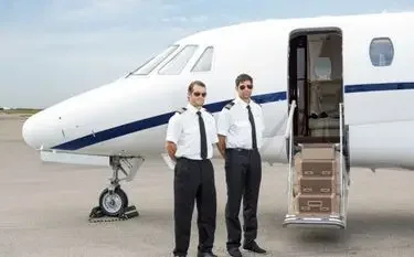 Professional pilots standing beside luxury private jet with open cabin door on airport tarmac