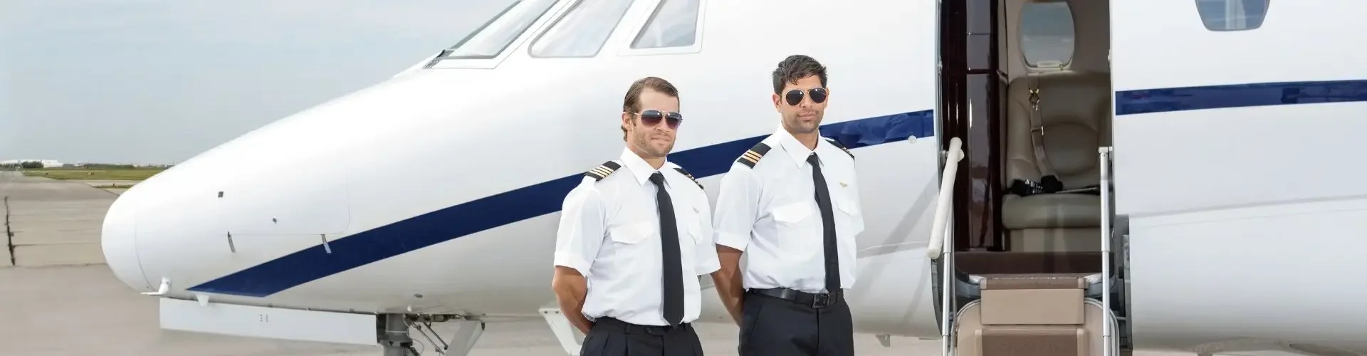 Professional pilots standing beside luxury private jet with open cabin door on airport tarmac