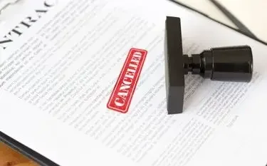 Red cancelled stamp on contract document with rubber stamp beside it on wooden desk surface