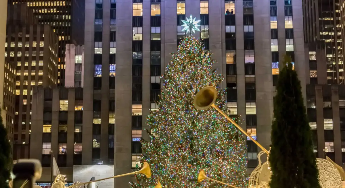 Rockefeller Center Christmas tree illuminated at night surrounded by Manhattan skyscrapers and golden angels