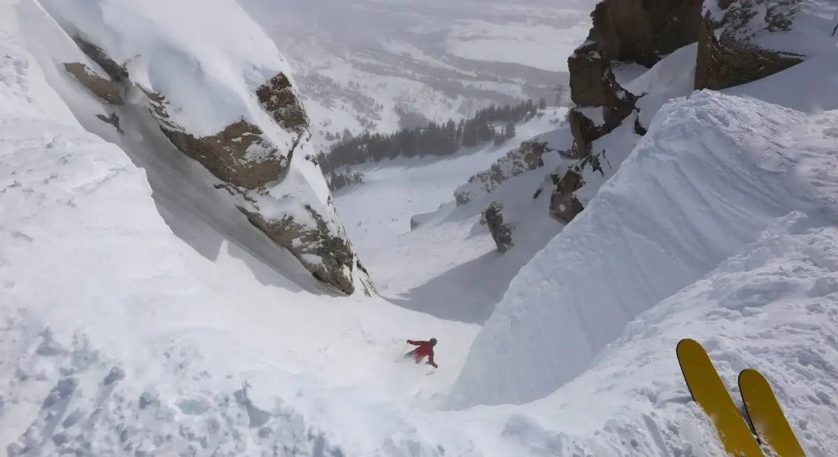 Skier carving through pristine powder snow between dramatic alpine cliffs at exclusive mountain resort