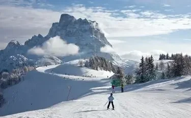 Top Ski Resorts to Visit by Private Jet This Winter Skier descending pristine Alpine slopes with dramatic snow-capped mountain peaks and evergreen forests