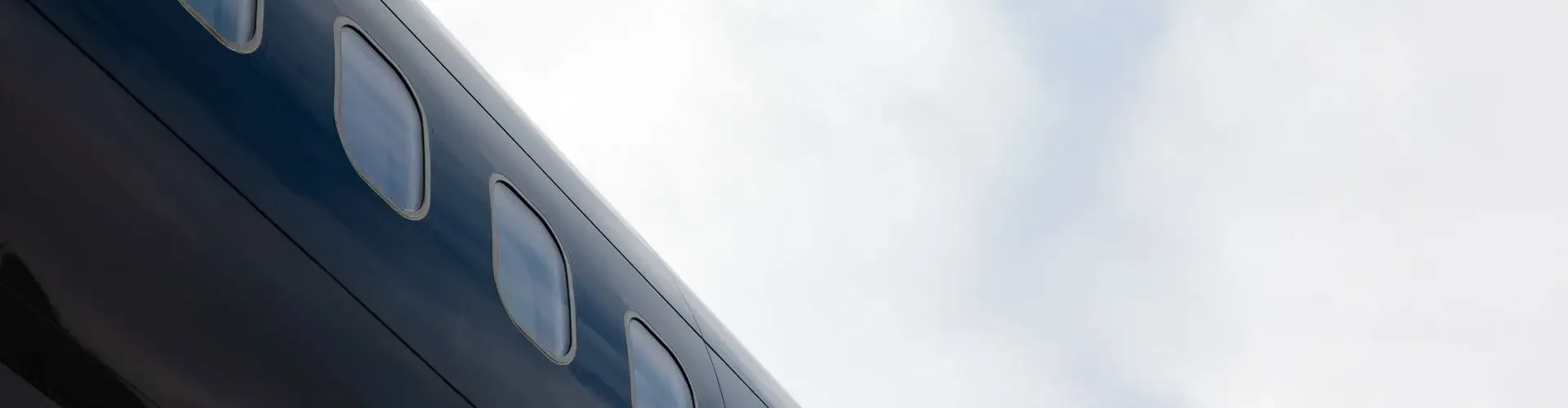 Sleek private jet fuselage with passenger windows viewed from below against cloudy sky backdrop