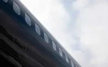 Sleek private jet fuselage with passenger windows viewed from below against cloudy sky backdrop