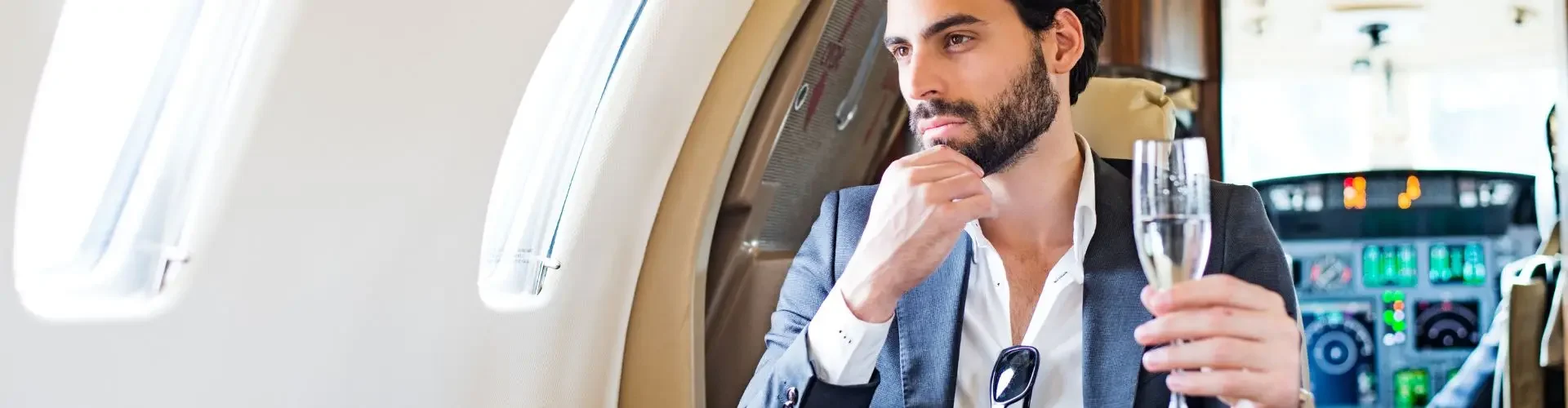 Booking a Private Jet for Business Travel in the UK Professional businessman enjoying champagne while working on laptop during luxury private jet flight