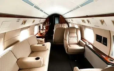Spacious private jet cabin interior featuring cream leather seats and polished wood accents for luxury travel