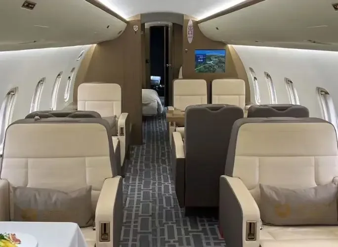 Spacious private jet cabin interior featuring cream leather seats and entertainment display for VIP travel