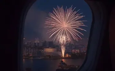 Spectacular fireworks display viewed through private jet window overlooking illuminated city skyline at night