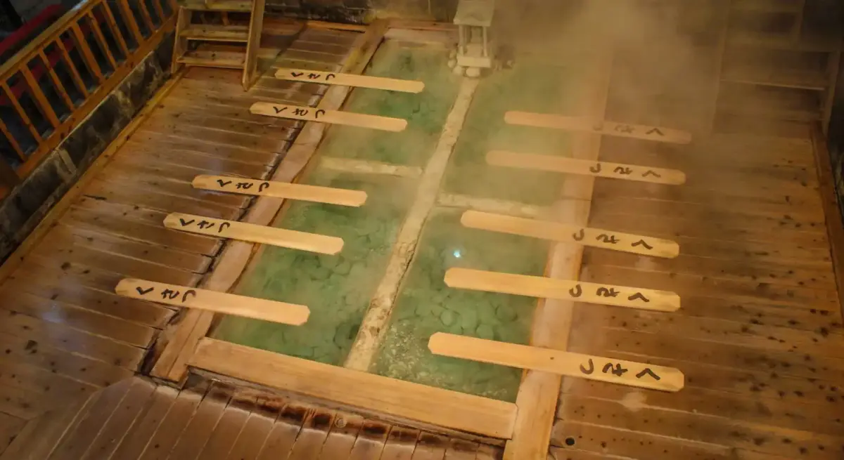 Traditional Japanese hot spring bath with wooden railings and mineral-rich green water for winter relaxation