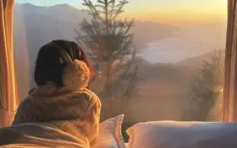 Traveler enjoying mountain sunrise from luxury accommodation window at exclusive ski resort destination