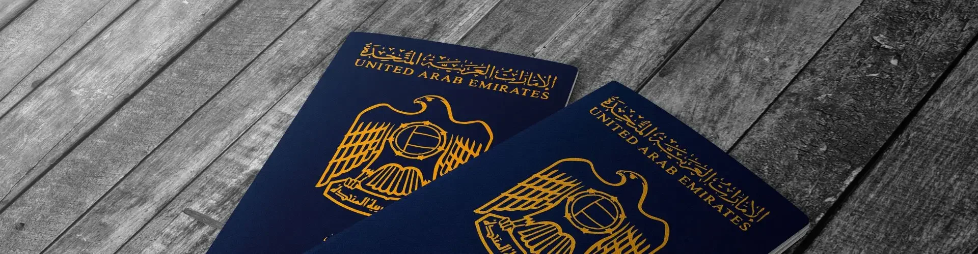 Two UAE passports with golden emblems displayed on weathered wooden surface for international travel