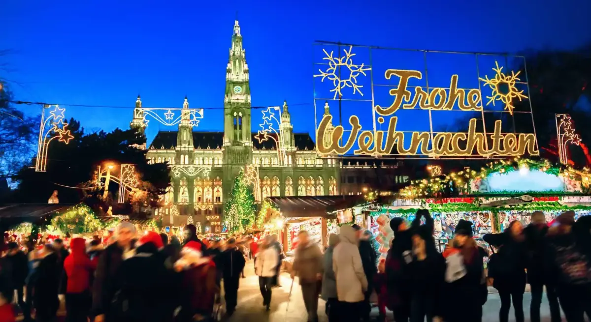 Vienna Christmas market bustling with visitors beneath illuminated Rathaus and festive Frohe Weihnachten sign