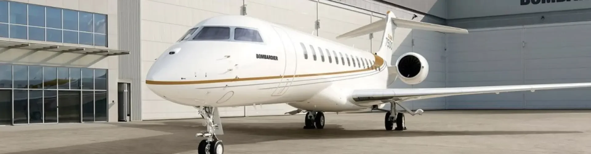 White private jet parked outside modern aviation hangar under blue sky with clouds
