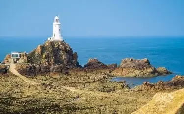 White lighthouse perched on rocky cliffs overlooking turquoise waters near Jersey coastline