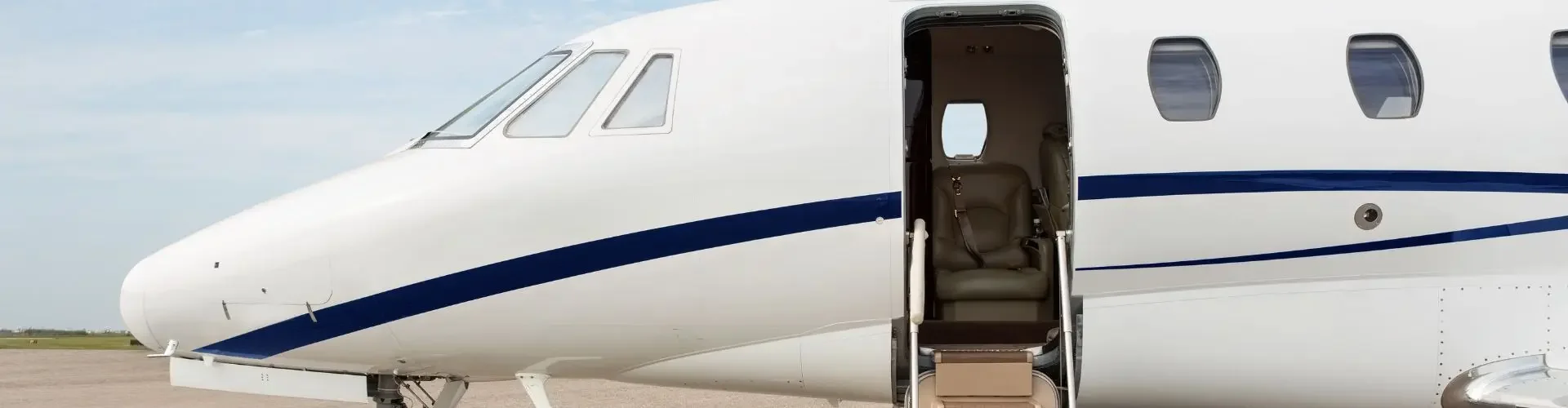 White private jet with open cabin door and boarding stairs on tarmac under cloudy sky