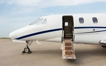 White private jet with open cabin door and boarding stairs on tarmac under cloudy sky