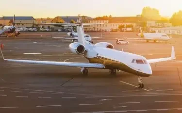 White private jet parked on airport tarmac during golden hour sunset with terminal buildings visible