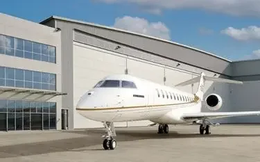 White private jet parked outside modern aviation hangar under blue sky with clouds
