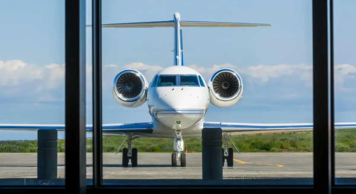 White private jet parked on tarmac viewed through terminal window, showcasing speed-focused design