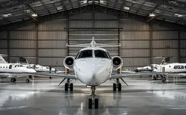 White private jet positioned in modern aircraft hangar with additional jets visible in background