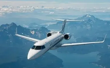 White private jet soaring above snow-capped Canadian mountain ranges under cloudy blue skies