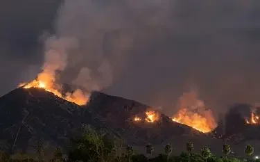 Wildfire flames and smoke engulfing mountainous terrain during climate disaster emergency evacuation scenario
