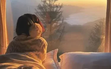 Top Winter Destinations to Visit by Private Jet This Christmas Woman in cozy sweater enjoying warm coffee while gazing at snowy winter landscape through cabin window