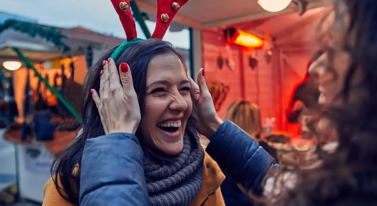 Woman laughing joyfully at Christmas market with festive lights and holiday atmosphere in background