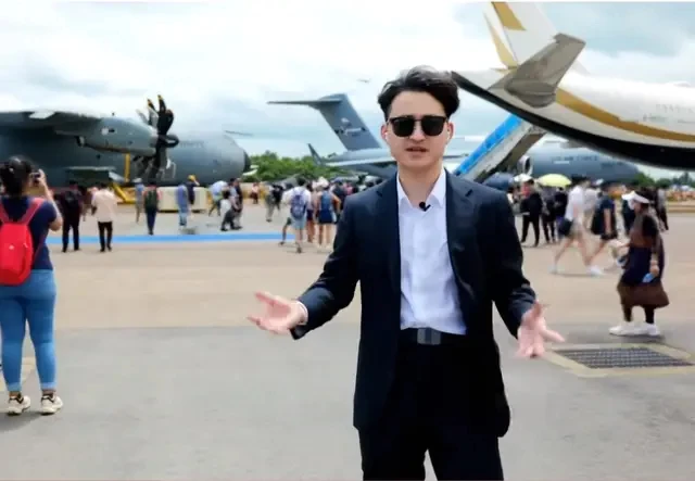 Well-dressed businessman gesturing at aviation showcase with military and private aircraft display