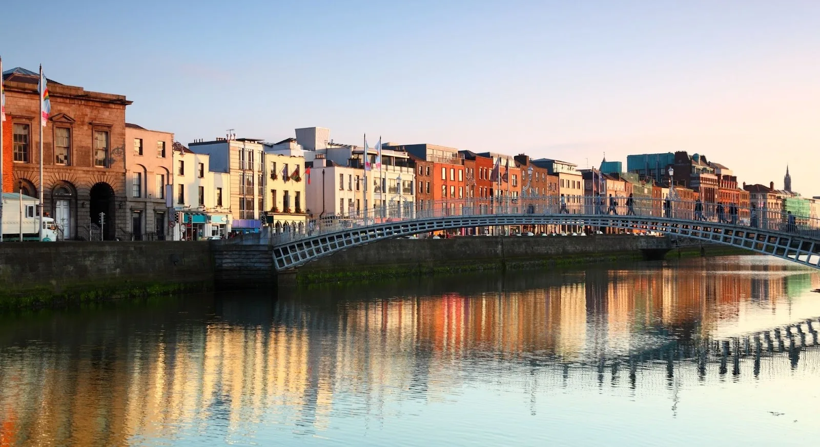 Dublin's Ha'penny Bridge spanning the River Liffey with colorful Georgian buildings reflecting in water at sunset