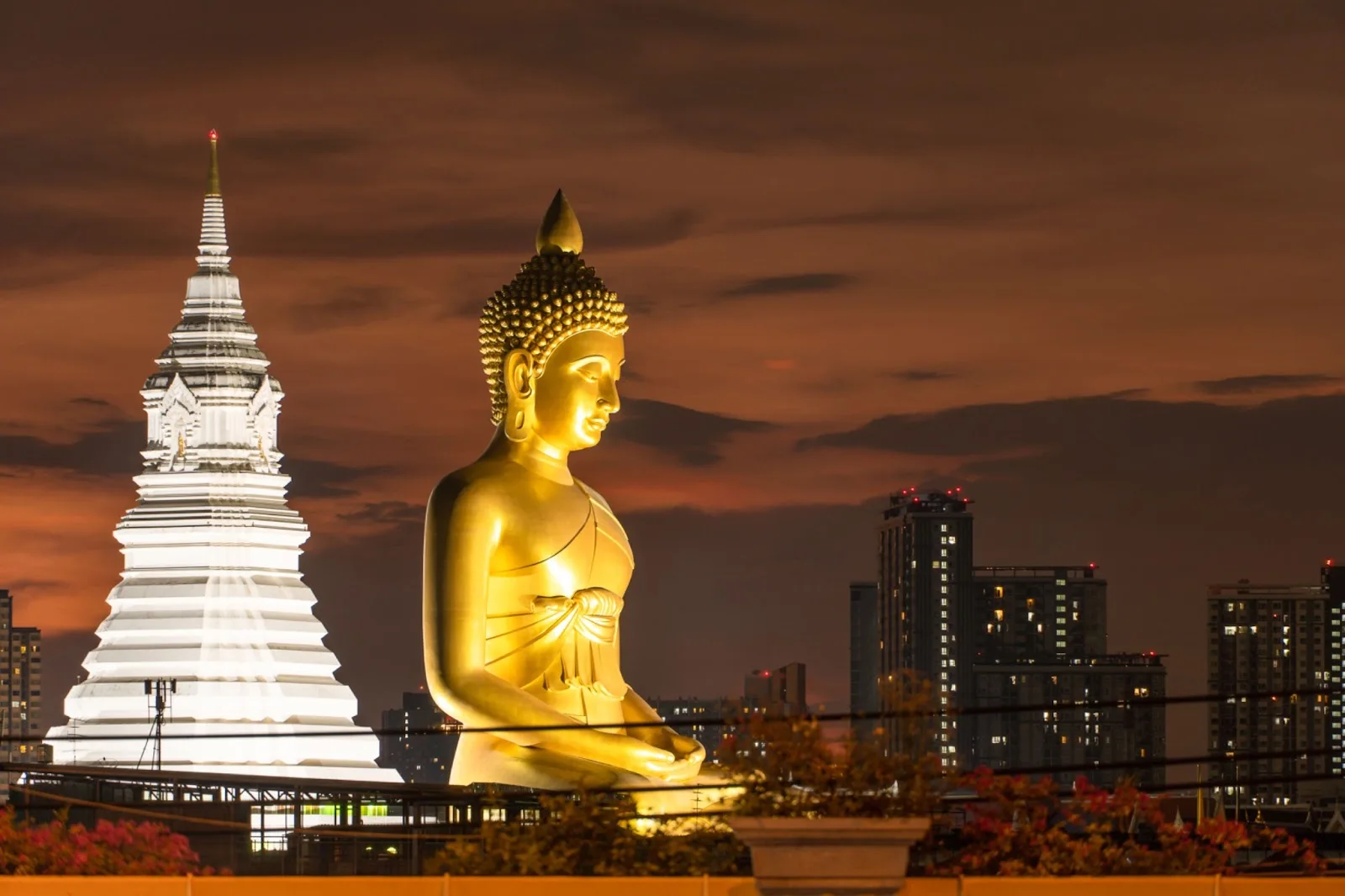 Golden Buddha statue and illuminated temple pagoda overlooking Bangkok skyline at dusk for luxury travel