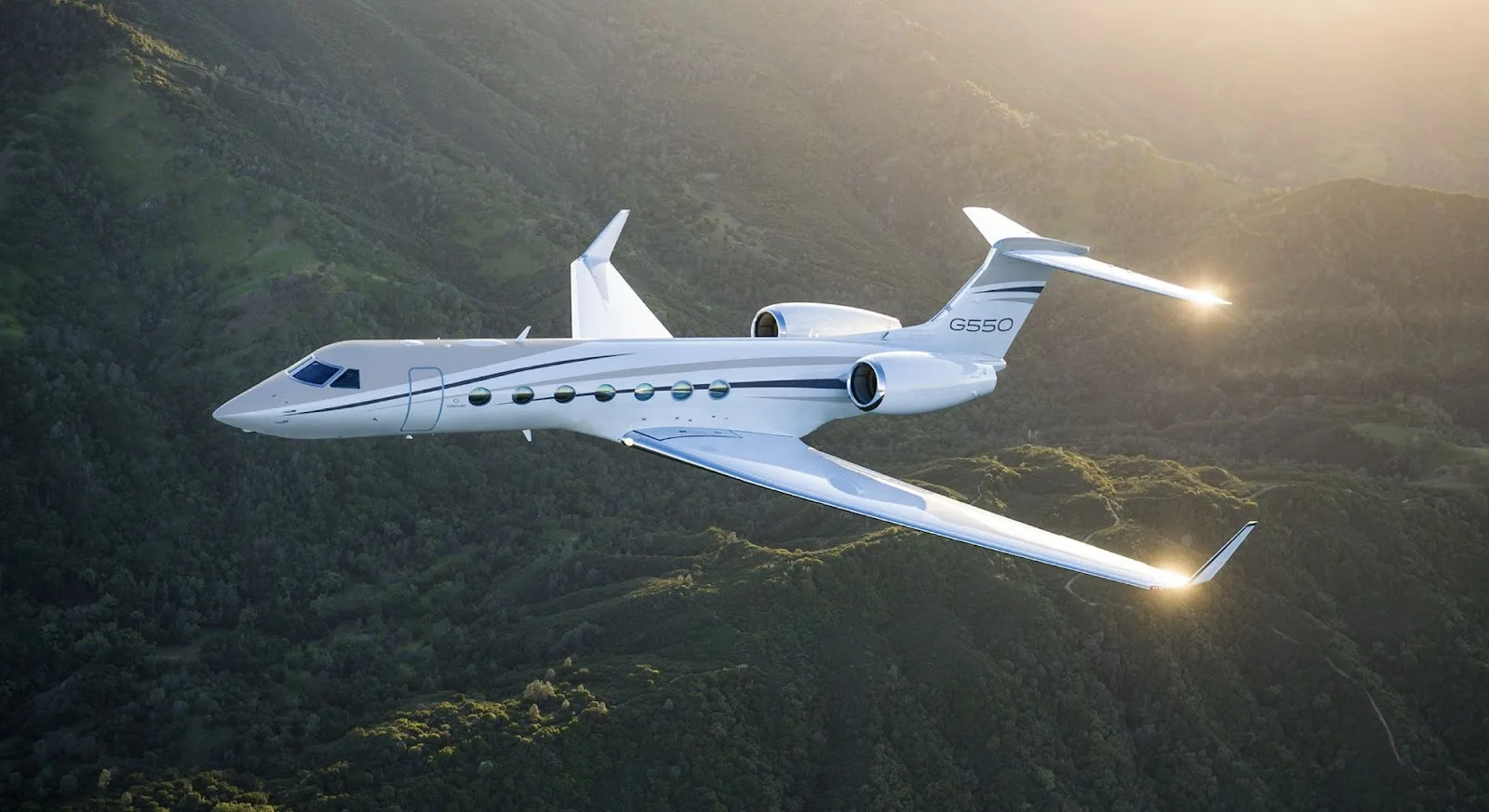 Gulfstream G550 private jet soaring over lush mountain terrain during golden hour flight conditions