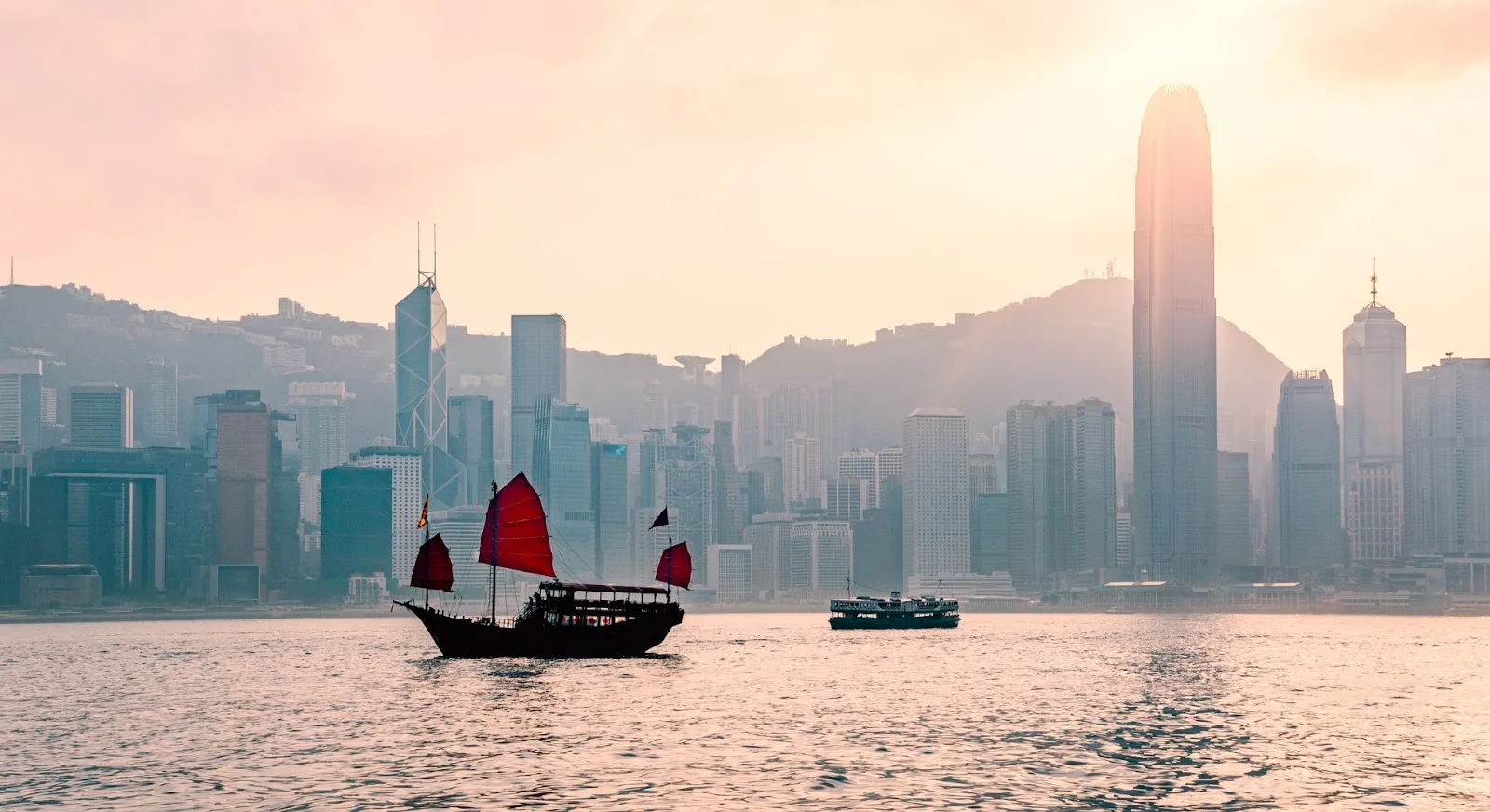 Traditional junk boat with red sails cruising Hong Kong harbor at sunset, showcasing luxury travel destination