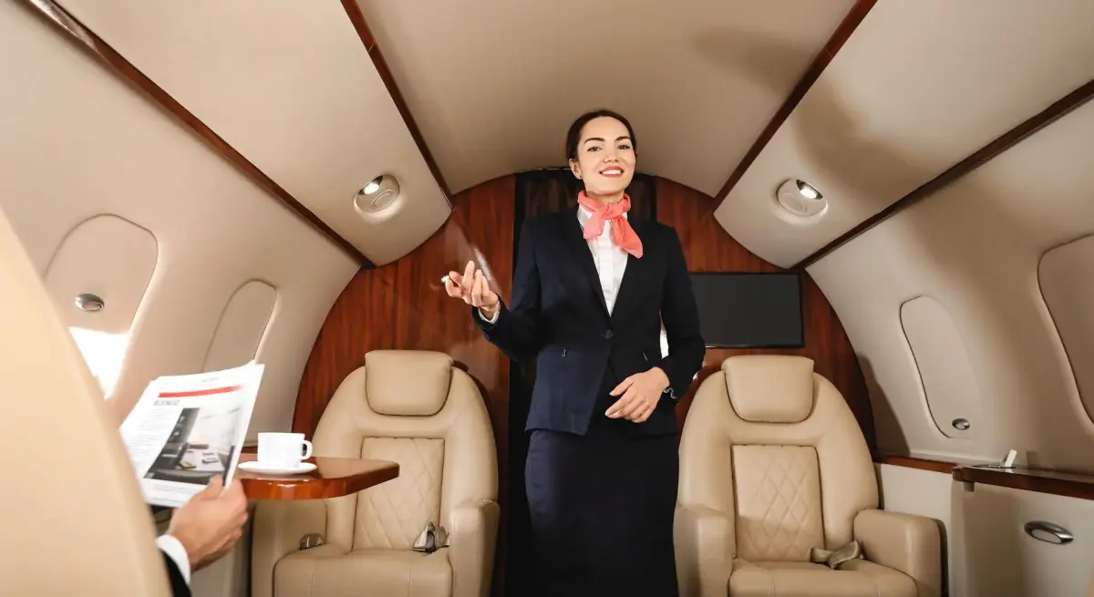 Professional flight attendant providing personalized service in luxury private jet cabin with leather seating