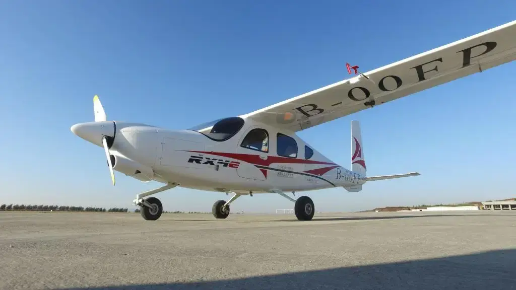 White RX4E electric aircraft with red accents parked on airport tarmac under clear blue sky