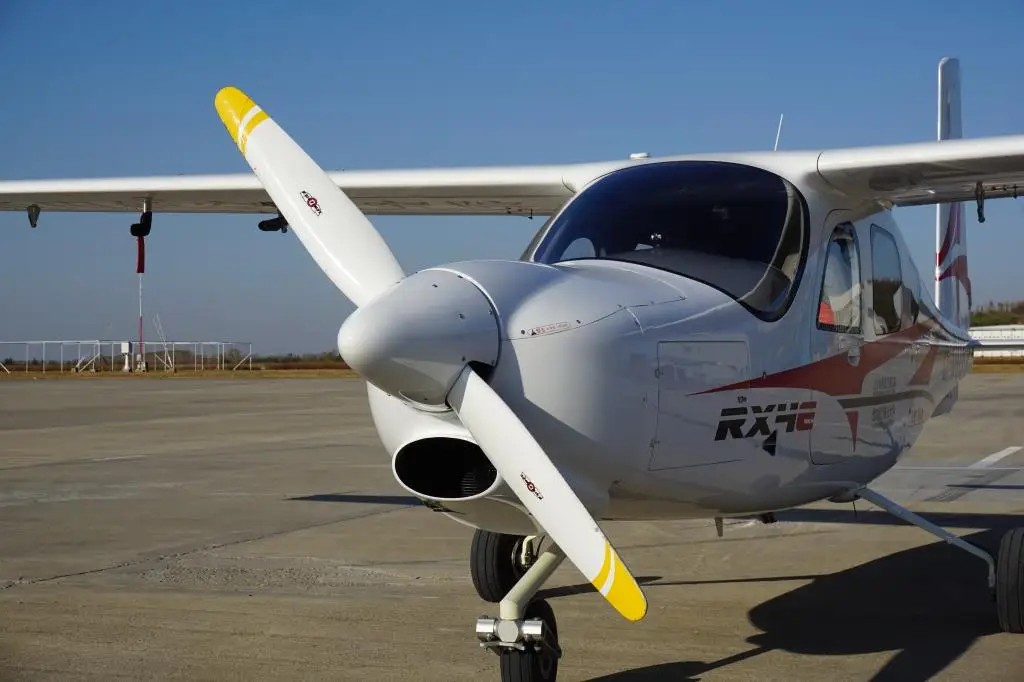 White RX4E electric aircraft with yellow propeller tips parked on airport tarmac under clear blue sky