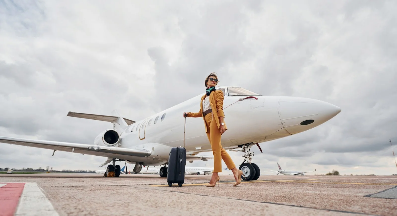 Stylish businesswoman with luggage walking confidently beside white private jet on airport tarmac