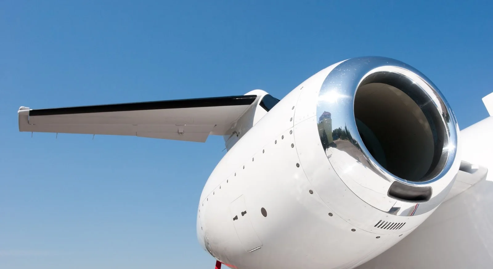 Close-up view of white private jet engine and wing against clear blue sky showcasing aircraft engineering