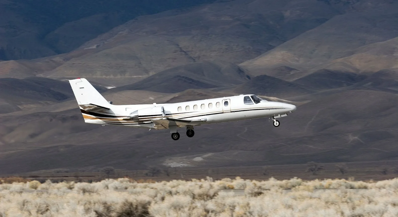 White private jet flying low over desert landscape, demonstrating empty leg charter flight opportunities